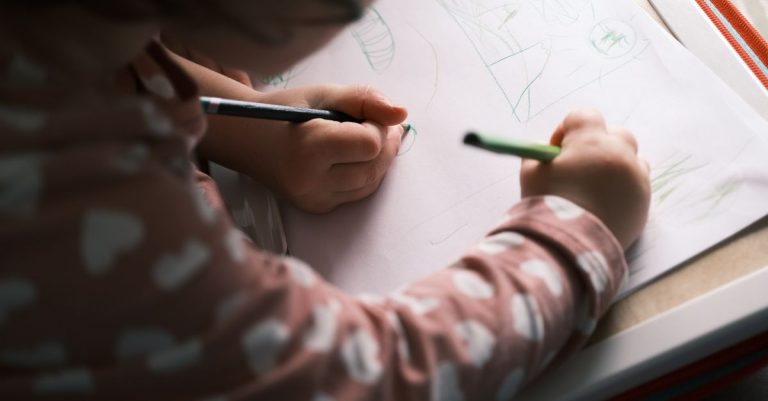 Reposo en cama con un niño de 4 años: cómo sobrevivir sin perder la calma 5 A young child drawing with colored pencils, capturing creativity and concentration in soft lighting indoors.