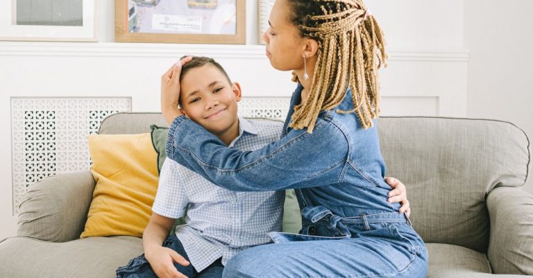 A woman with braids embraces her son on a sofa, creating a warm family moment.
