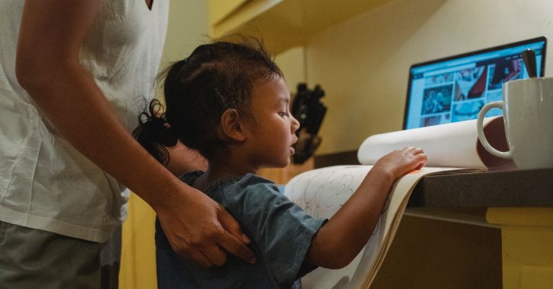 No es berrinche, es miedo: Cuando tu hijo llora por cada error 3 Side view of attentive little ethnic girl showing album with drawings to crop faceless young mother working remotely in laptop at home