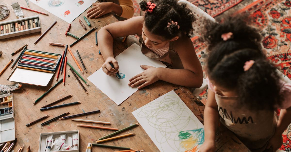 Children drawing with colored pencils and papers indoors, showcasing creativity.