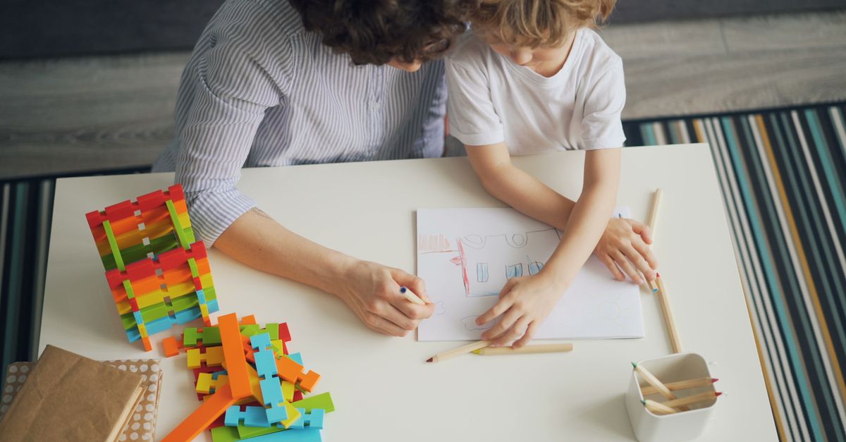 A mother and son enjoying a creative drawing session with colorful blocks at home.